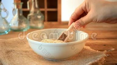 女人的手正在倒干藜麦<strong>颗粒</strong>，在木制<strong>厨房</strong>桌子上有勺子。